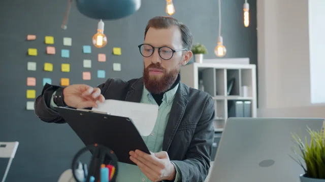 A focused young man with glasses reviewing documents in a stylish, modern office setting. Reviewing reputation services by comparing only the overlapping job