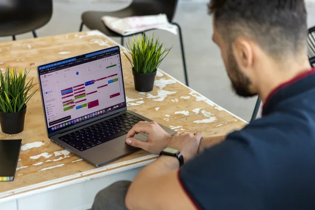 Man working remotely at a desk with a laptop open to a calendar app. Reputation management supplier comparison: four review-response routes on one job ticket